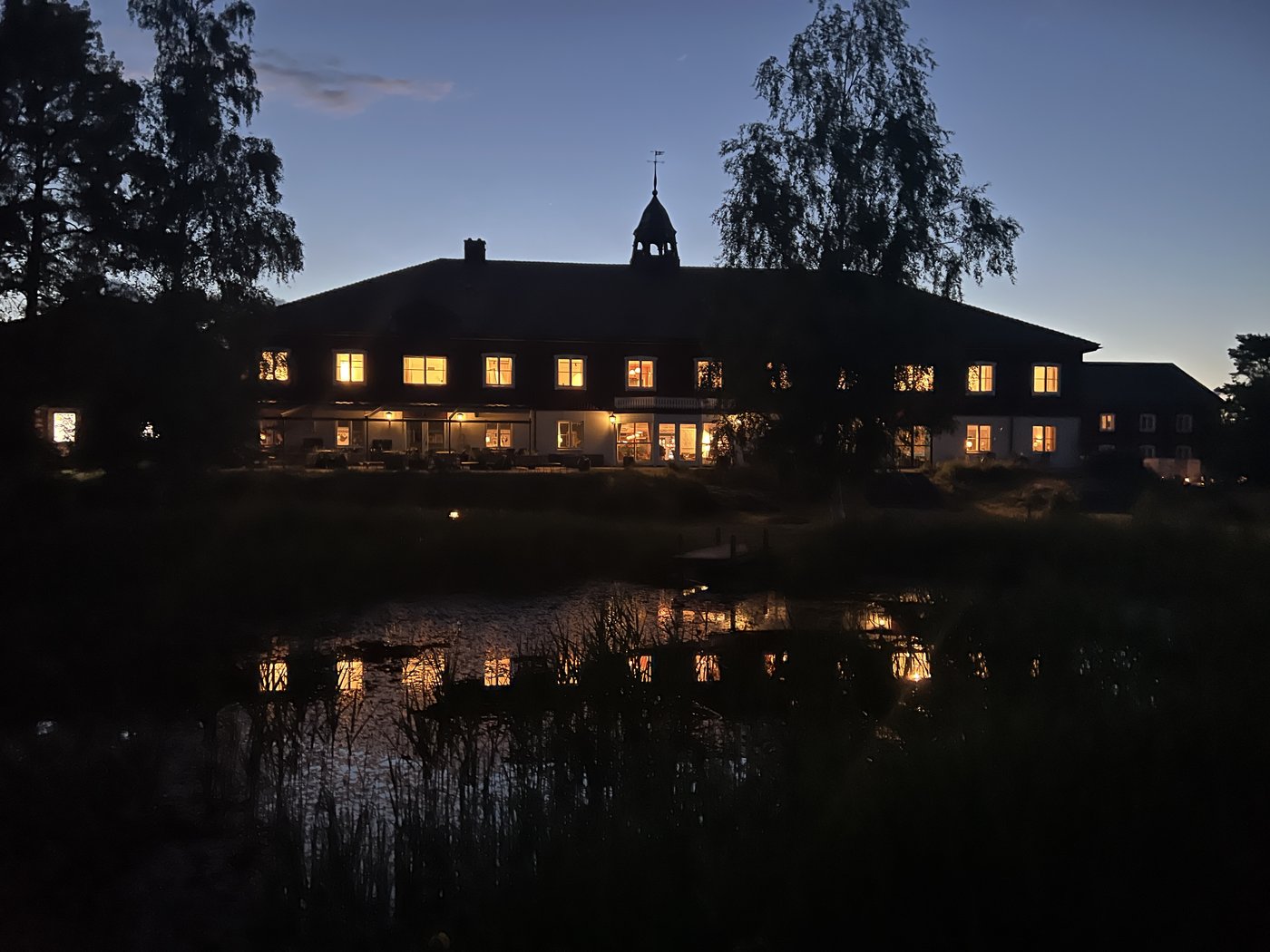 Fågelbro värdshus upplyst i skymningen, speglat i vattnet